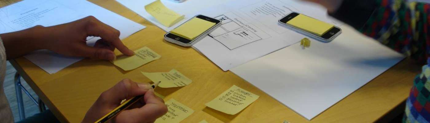 Multiple people at a table sketching on PostIt notes